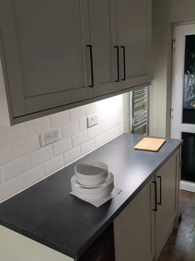A sage shaker kitchen with under-cabinet lighting and sockets set into the tiles, wired by Harry Radford